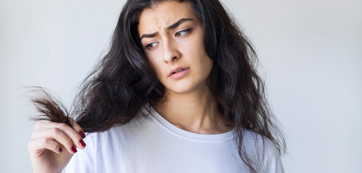 Frau blickt verzweifelt auf ihre trockenen schwarzen Haare.